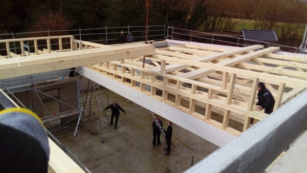 Holzkonstruktion eines neuen Gebäudes in der Bauphase, mit mehreren Handwerkern, die an der Montage der Deckenkonstruktion arbeiten.